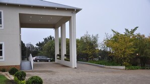 A covered parking area with a paved driveway leading to a building entrance, surrounded by greenery and trees. - Vetho 2 Apartments OR Tambo Airport (Kempton Park)