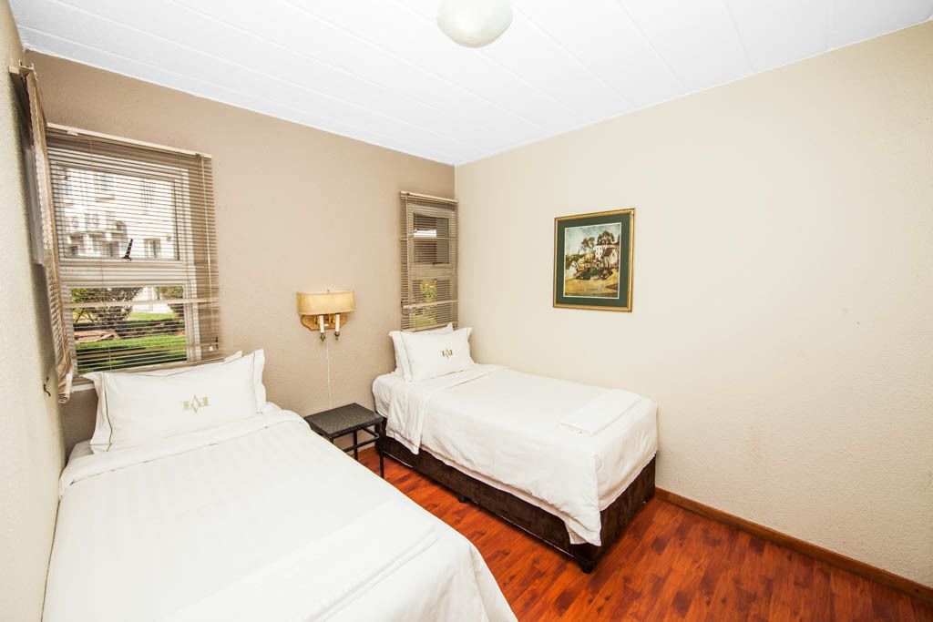A hotel room with two beds, a nightstand, a lamp, and a framed picture on the wall.