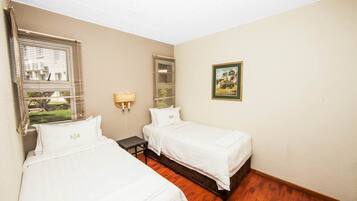 A hotel room with two beds, a nightstand, a lamp, and a framed picture on the wall.