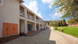 A building with a paved walkway, a grassy area, and a tree. - Vetho 2 Apartments OR Tambo Airport (Kempton Park)