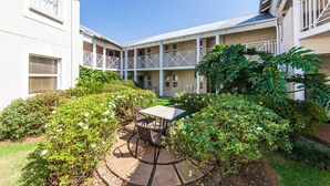 A courtyard with a table and chairs, surrounded by greenery and a building with balconies. - Vetho 2 Apartments OR Tambo Airport (Kempton Park)