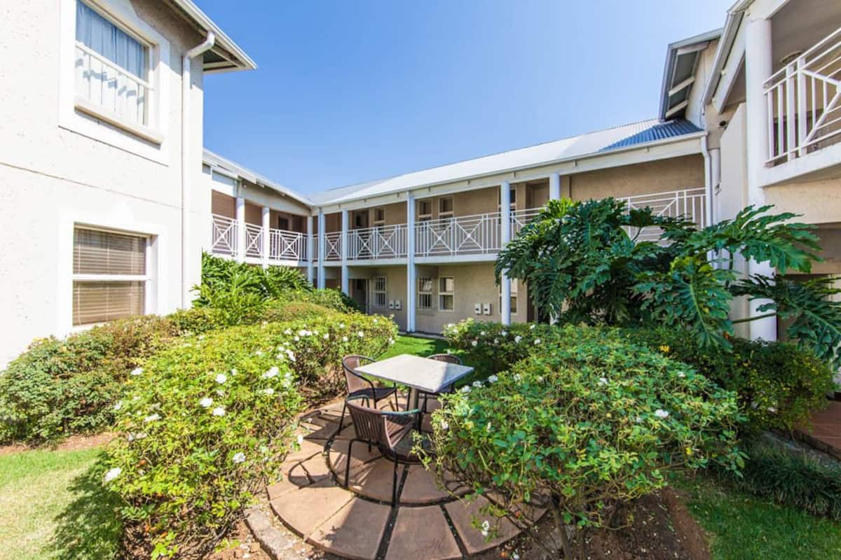 A courtyard with a table and chairs, surrounded by greenery and a building with balconies.
