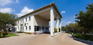 A building with a covered entrance, a paved driveway, and a small parking area. - Vetho 2 Apartments OR Tambo Airport (Kempton Park)