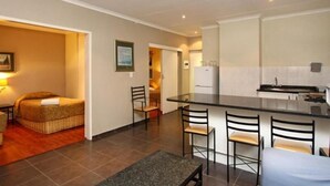 A compact hotel room with a kitchenette, a small dining area, and a bed with a headboard. - Vetho 2 Apartments OR Tambo Airport (Kempton Park)
