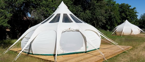 A white tent with a central window and a wooden platform, surrounded by trees.