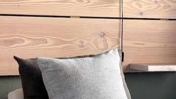 A neatly made bed with white sheets and two pillows, one dark and one light gray, against a wall with a wooden headboard.