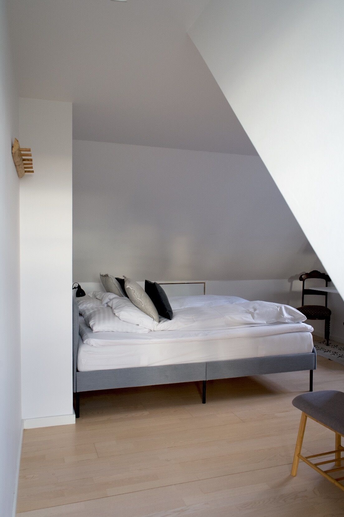 A modern bedroom with a sloped ceiling, a bed with white bedding, a wooden chair, and a small table.