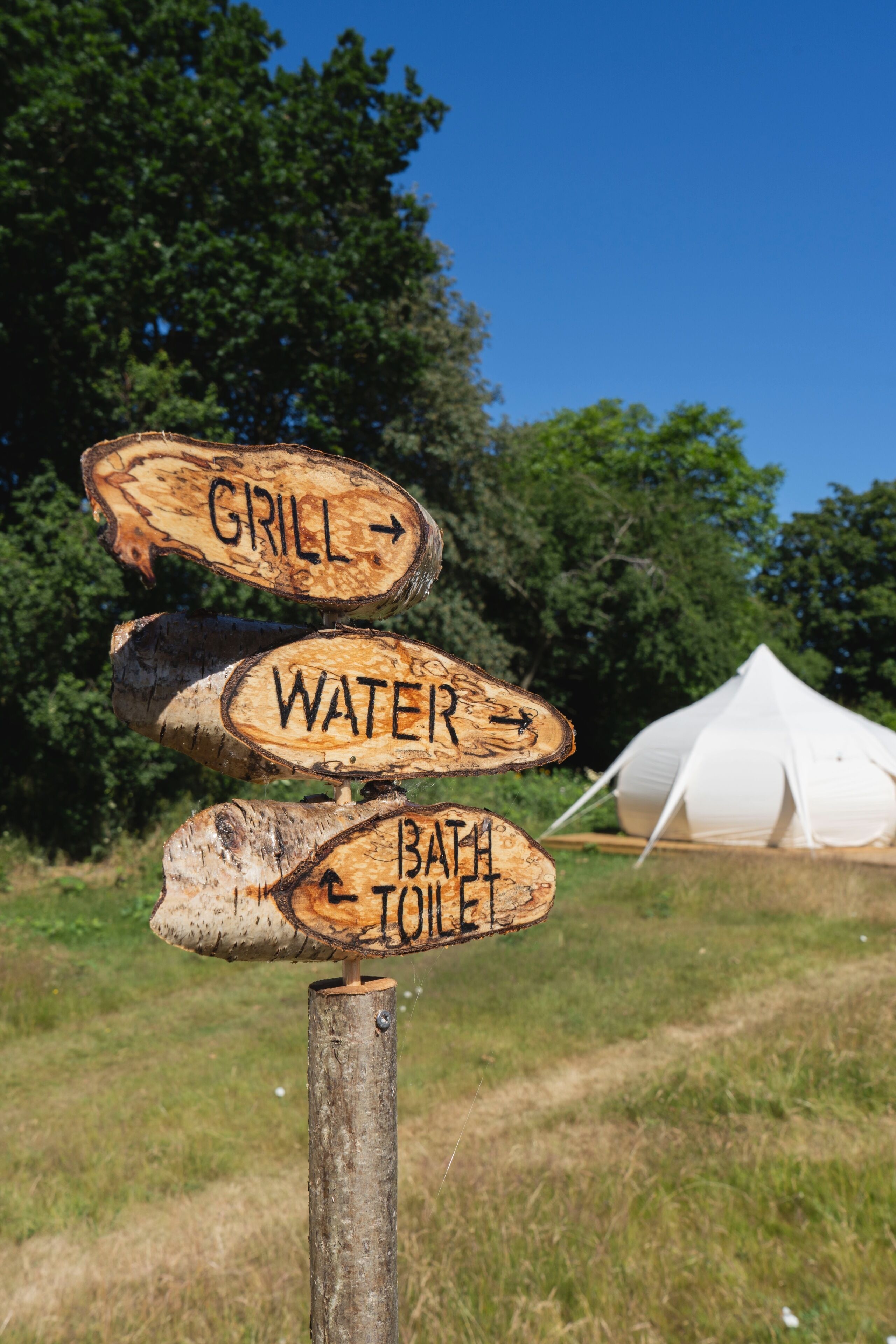 A wooden signpost with directional arrows pointing to amenities such as a grill, water, and bath/toilet.