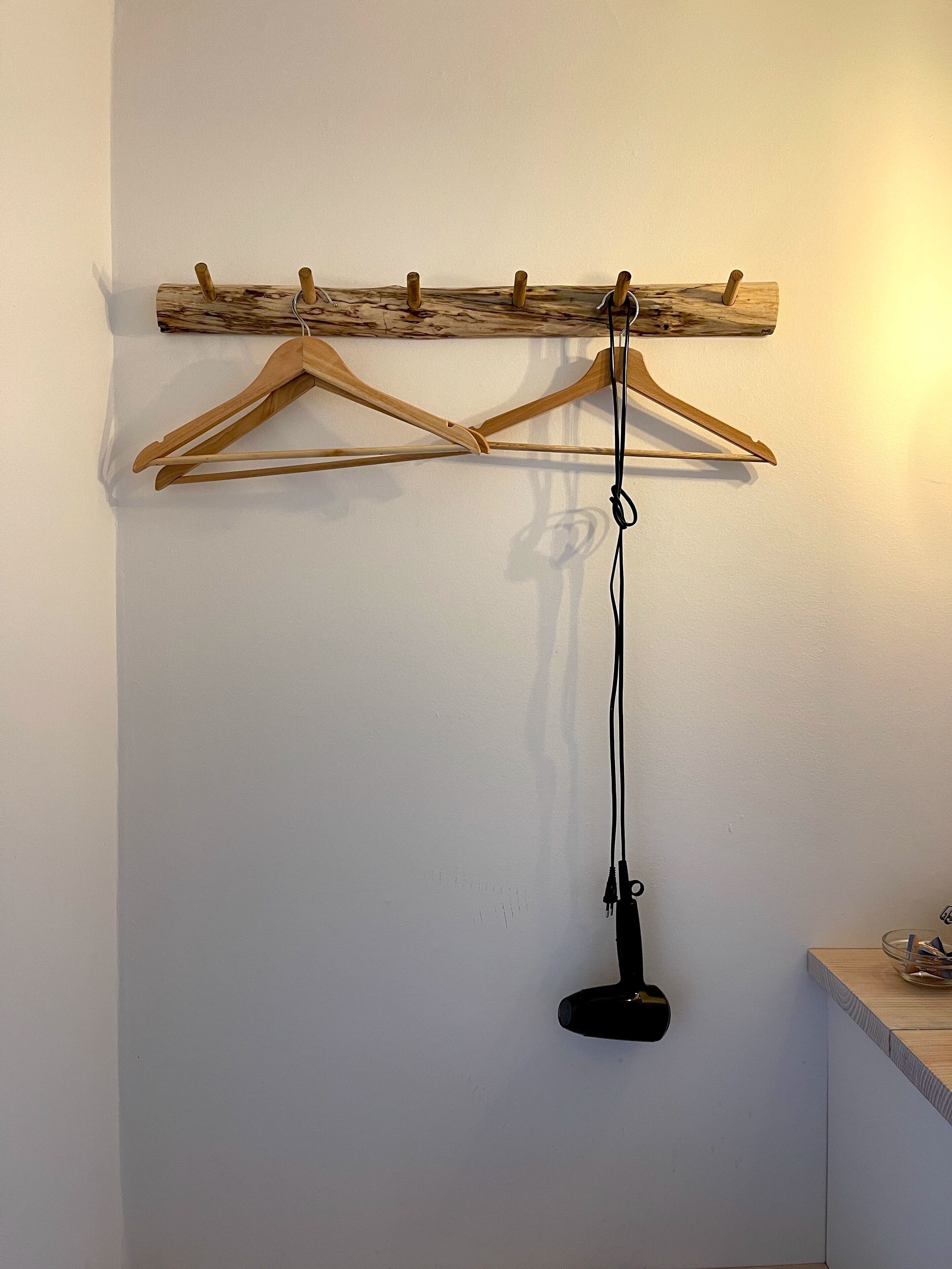 A wooden coat rack with multiple hangers against a white wall.