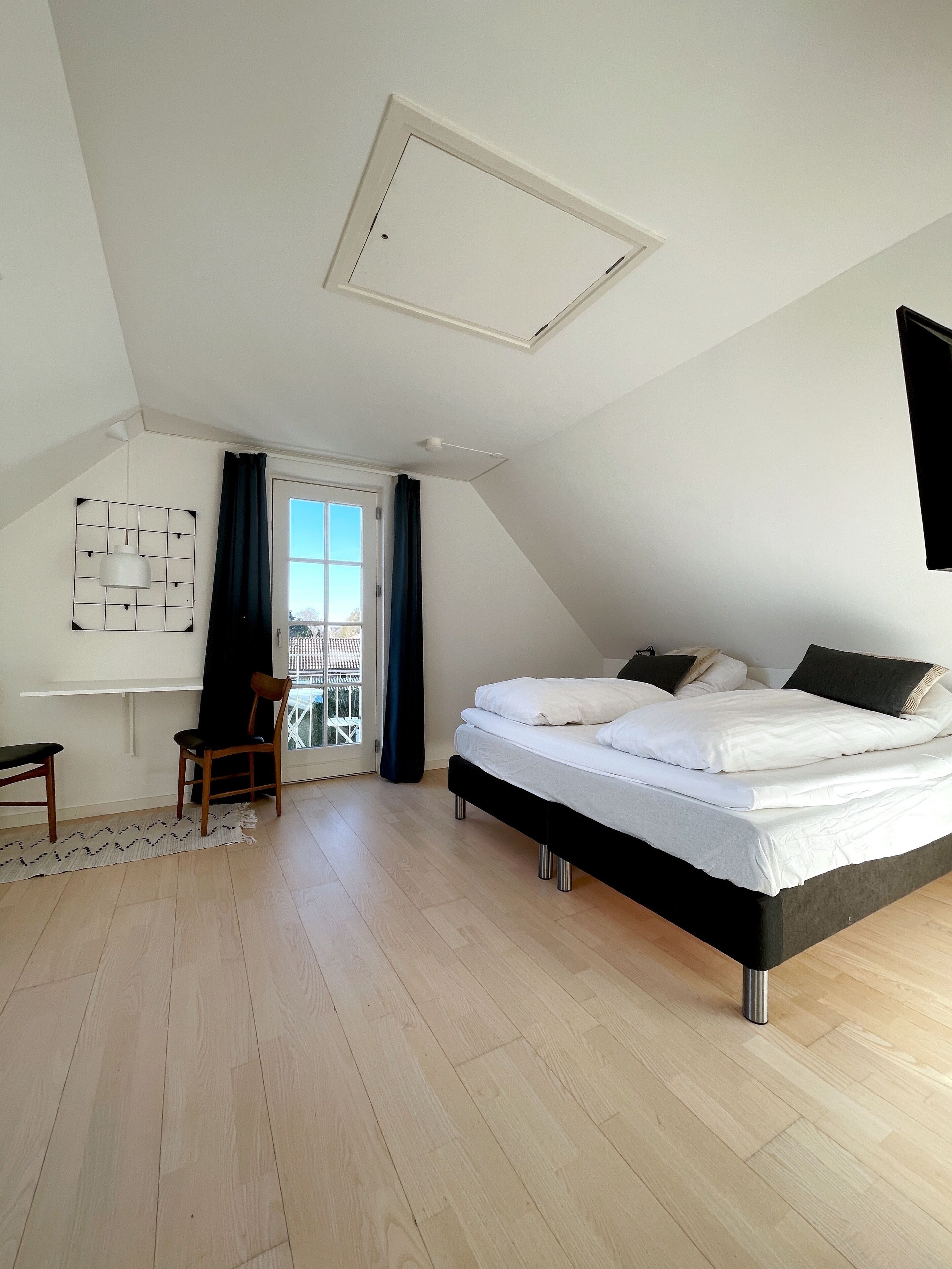 Un dormitorio con cama, una silla, un escritorio y una ventana con cortinas.