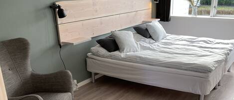 Un dormitorio con cama, dos sillas, cabecera de madera y ventana con cortinas.