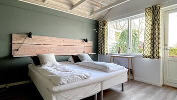 Un dormitorio con techo de madera, una cama con ropa de cama blanca, cabecera y una ventana con cortinas.