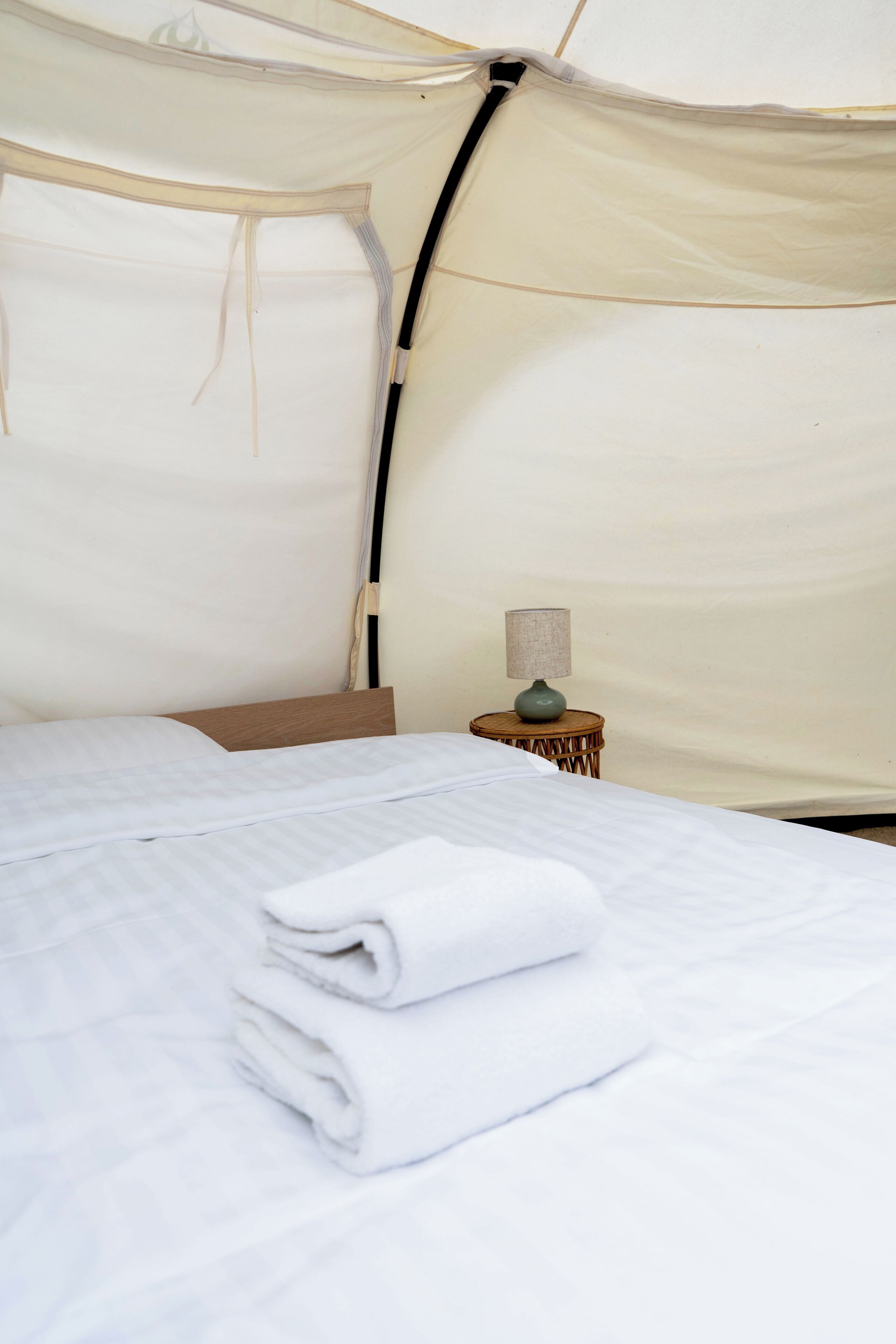 A tent-style room with a bed, a small table with a lamp, and a neatly folded towel.