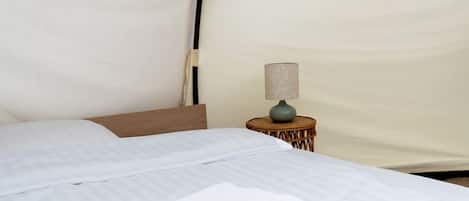 A tent-style room with a bed, a small table with a lamp, and a neatly folded towel.