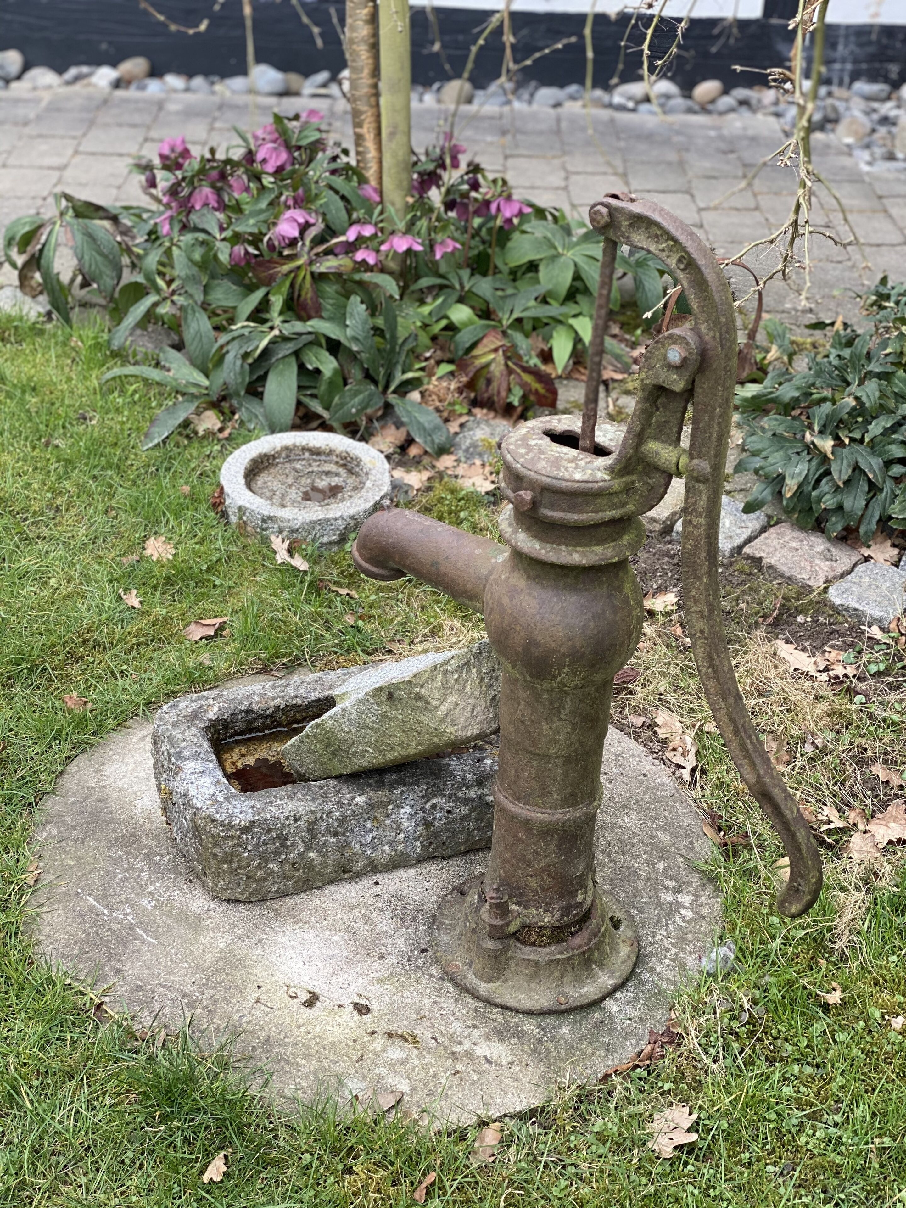 Une pompe à eau d’un autre âge, installée dans un jardin.
