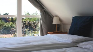 Un dormitorio con cama, lámpara y vista al exterior con vegetación.