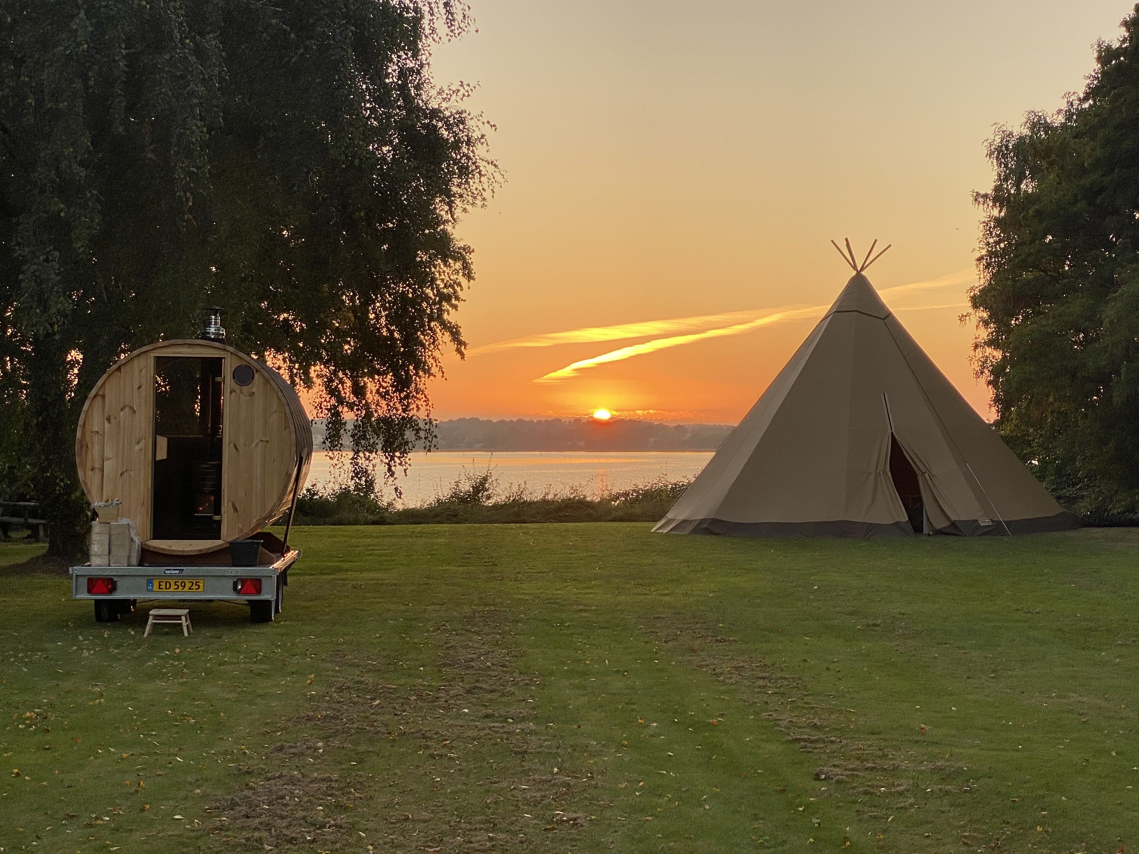Une yourte et une structure en bois au bord d’un lac, au coucher du soleil.
