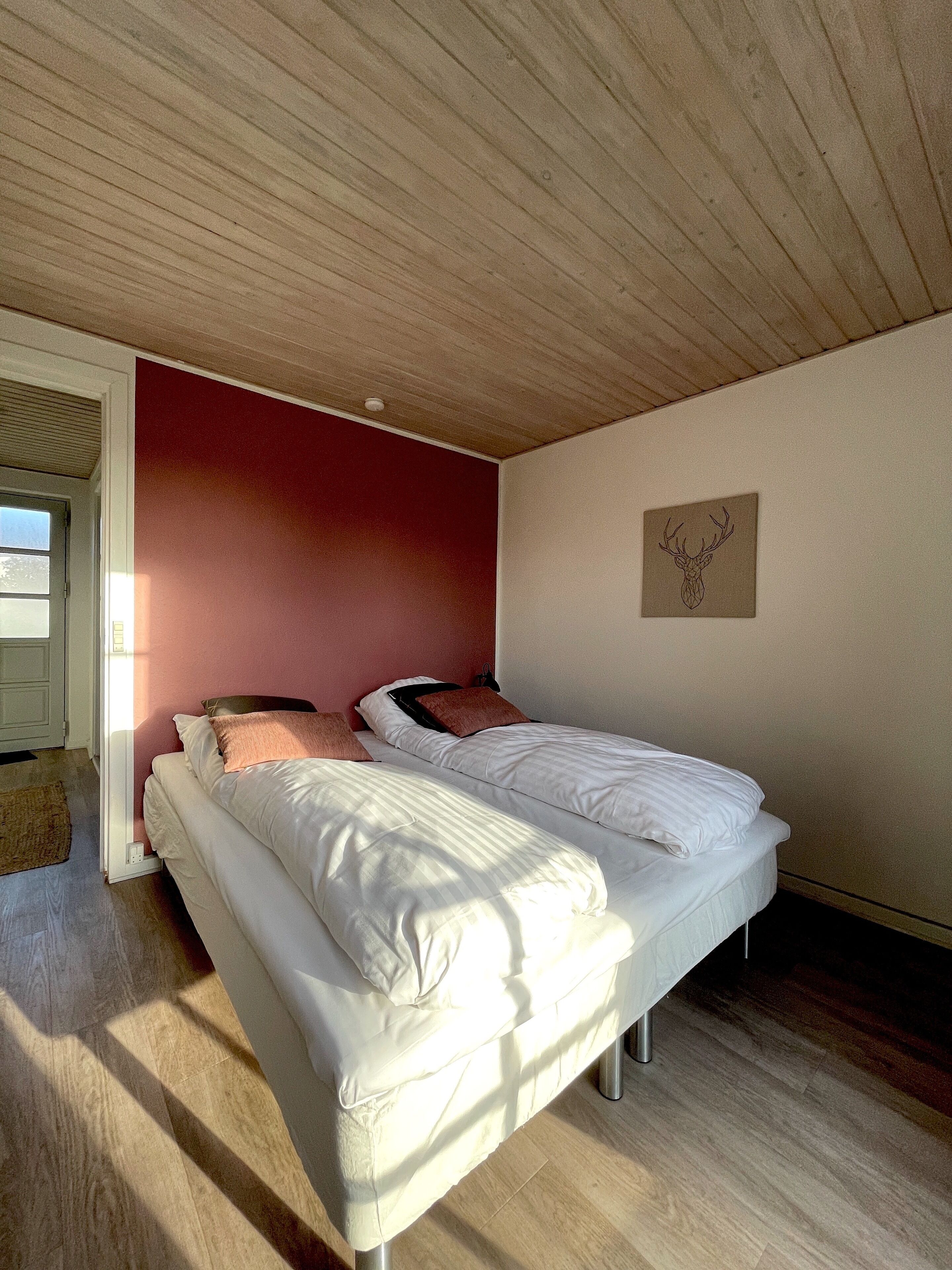 Ein Schlafzimmer mit einem Bett, einer roten Akzentwand und einem Bild von einem Hirschkopf.