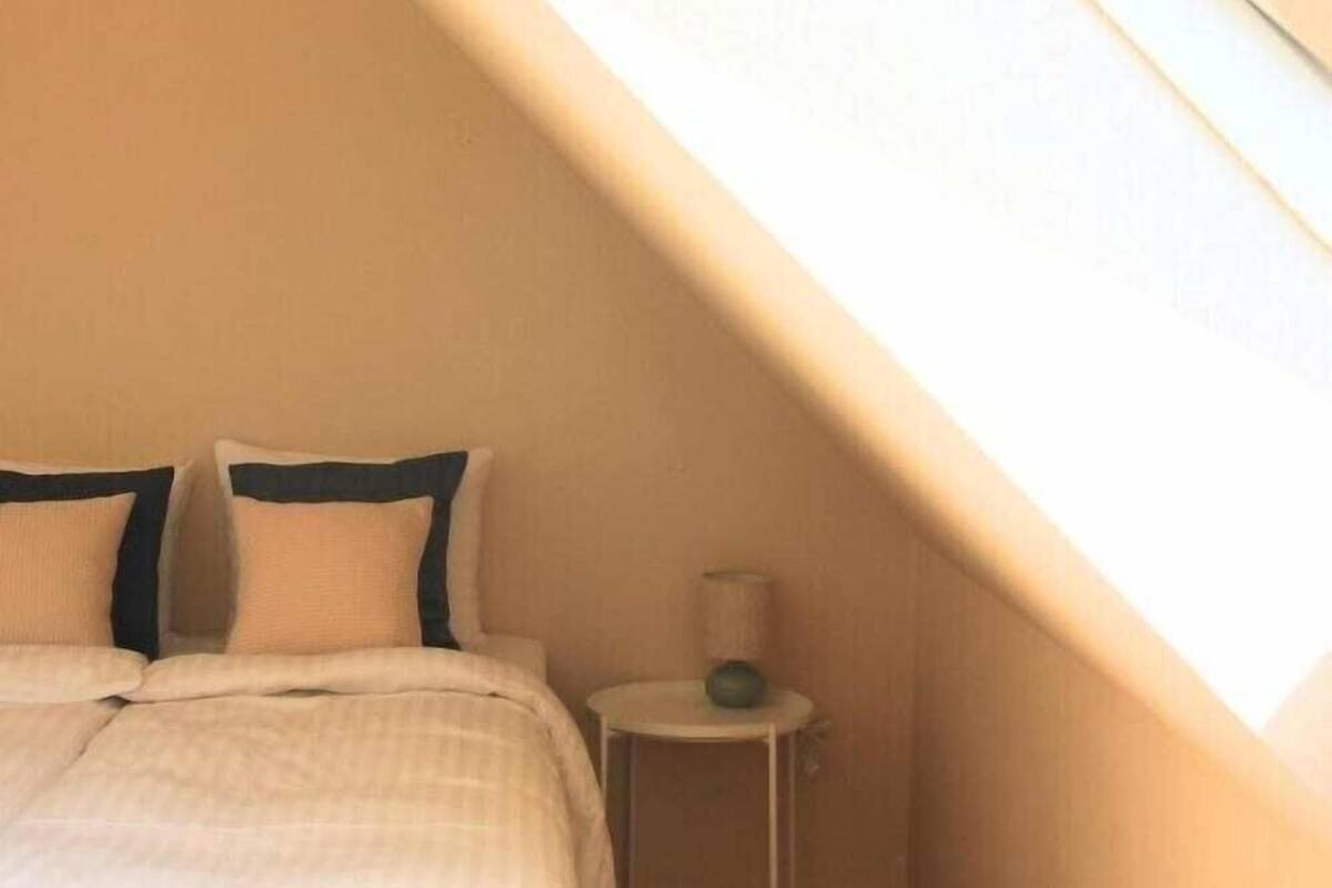 Une chambre à coucher avec un lit, des oreillers, une table de chevet avec une lampe et un plafond en pente.