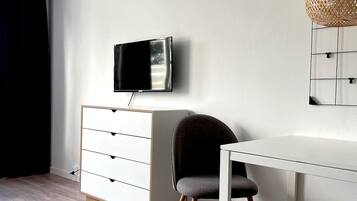 A modern room with a white desk, a grey chair, a white dresser, and a TV mounted on the wall.