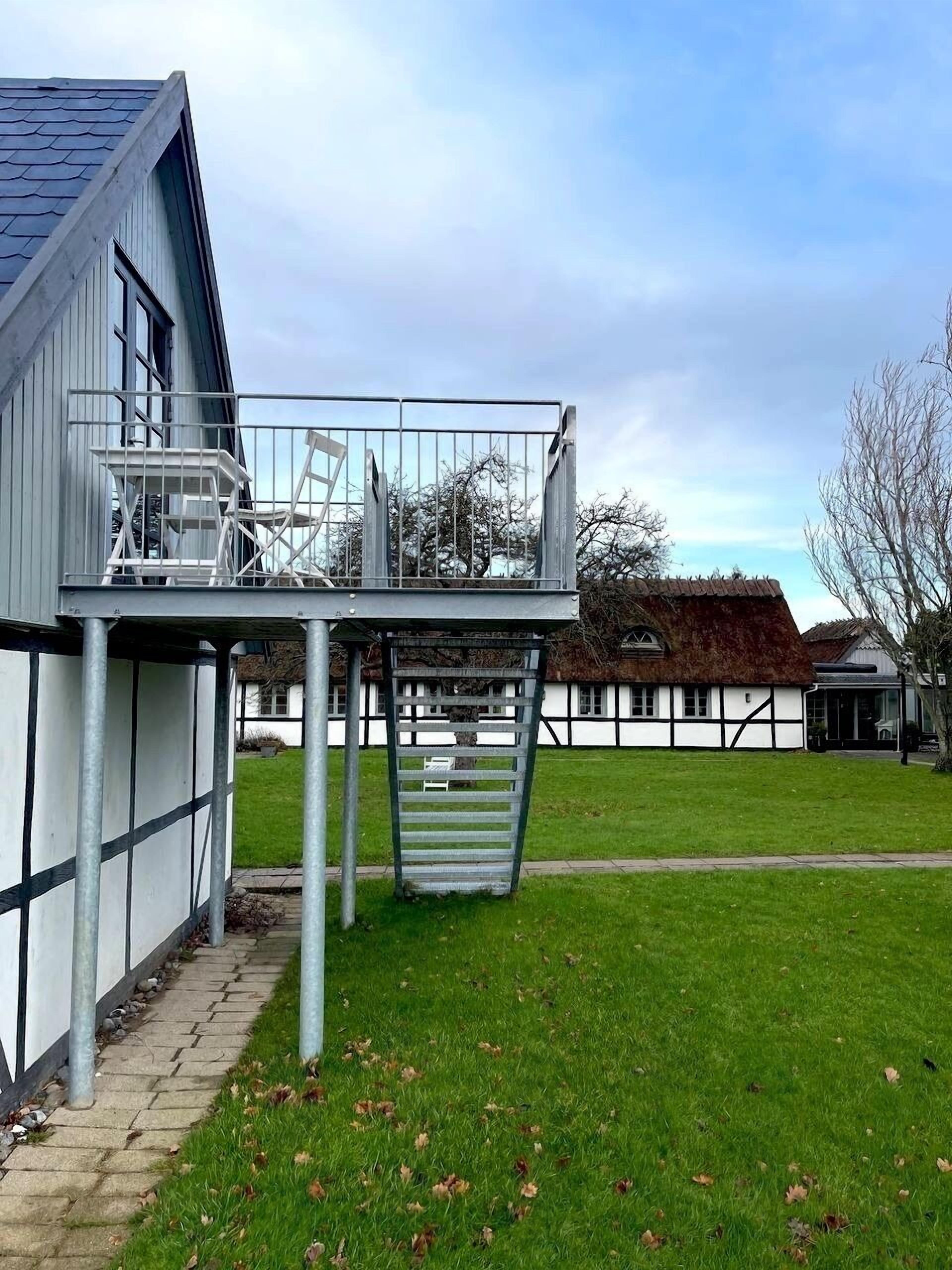 A building with a balcony, a staircase, and a grassy yard.