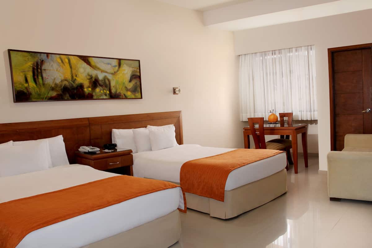 Habitación de hotel con dos camas, un cabecero de madera, un cuadro en la pared, un escritorio con una silla y una puerta.