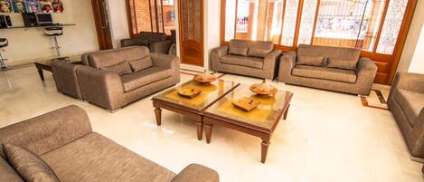 A spacious living room with multiple sofas and a coffee table, a bookshelf, and a large window with decorative glass panels.