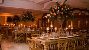 Une salle de banquet avec de longues tables dressées pour le repas, agrémentée de centres de table illuminés par des bougies et de chaises dorées.