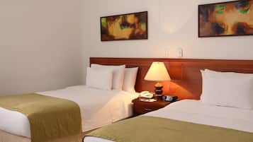 A hotel room with two beds, a wooden headboard, a bedside table with a lamp, and two paintings on the wall.