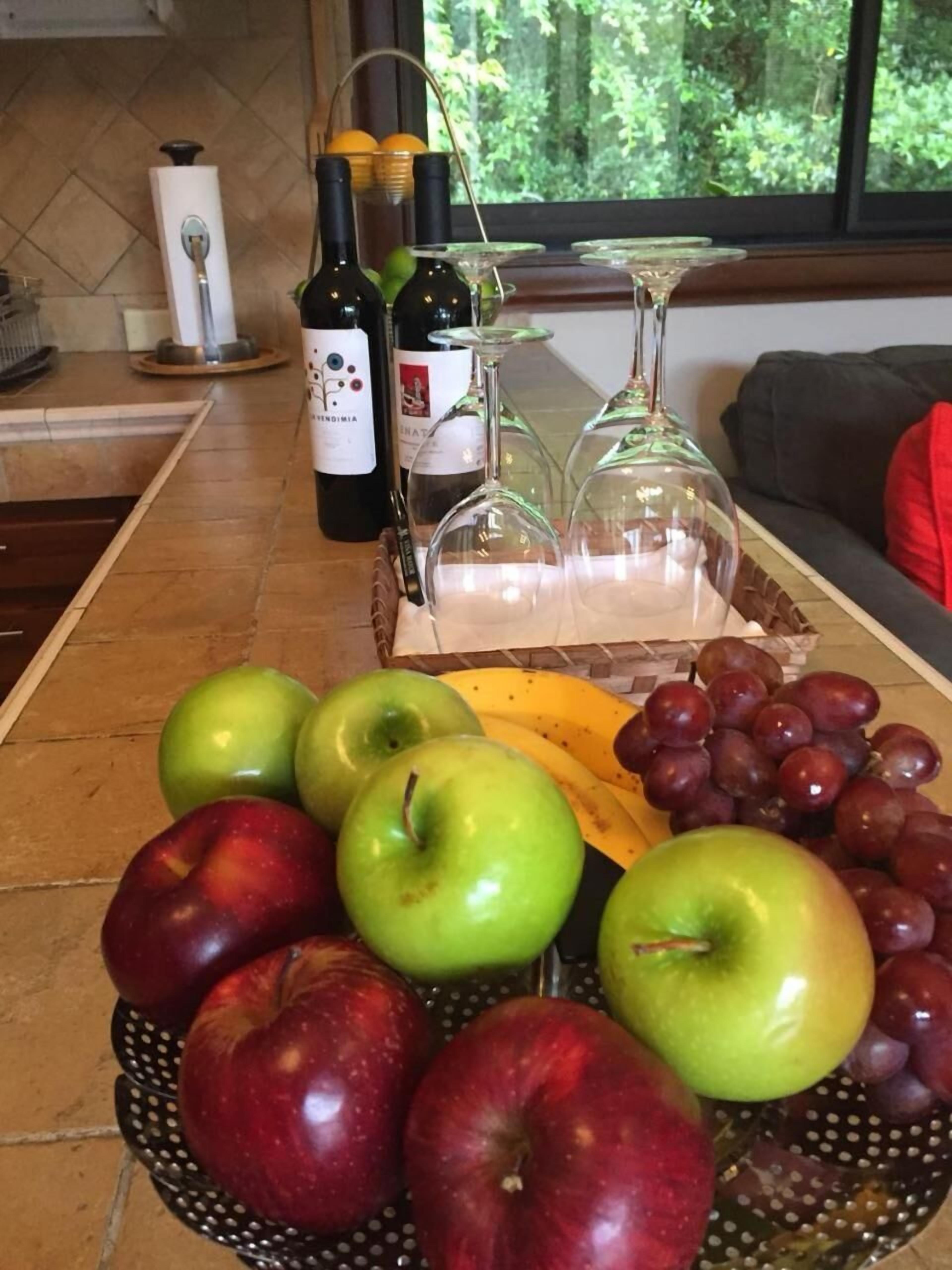 Eine Küchenarbeitsplatte mit einer Obstschale mit Äpfeln und Trauben, einem Bananenkorb und einer Weinflasche.