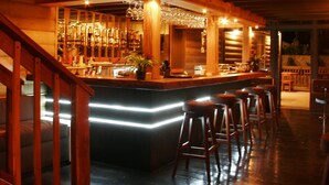 Zona de bar con baranda de madera, taburetes y mostrador con vasos.