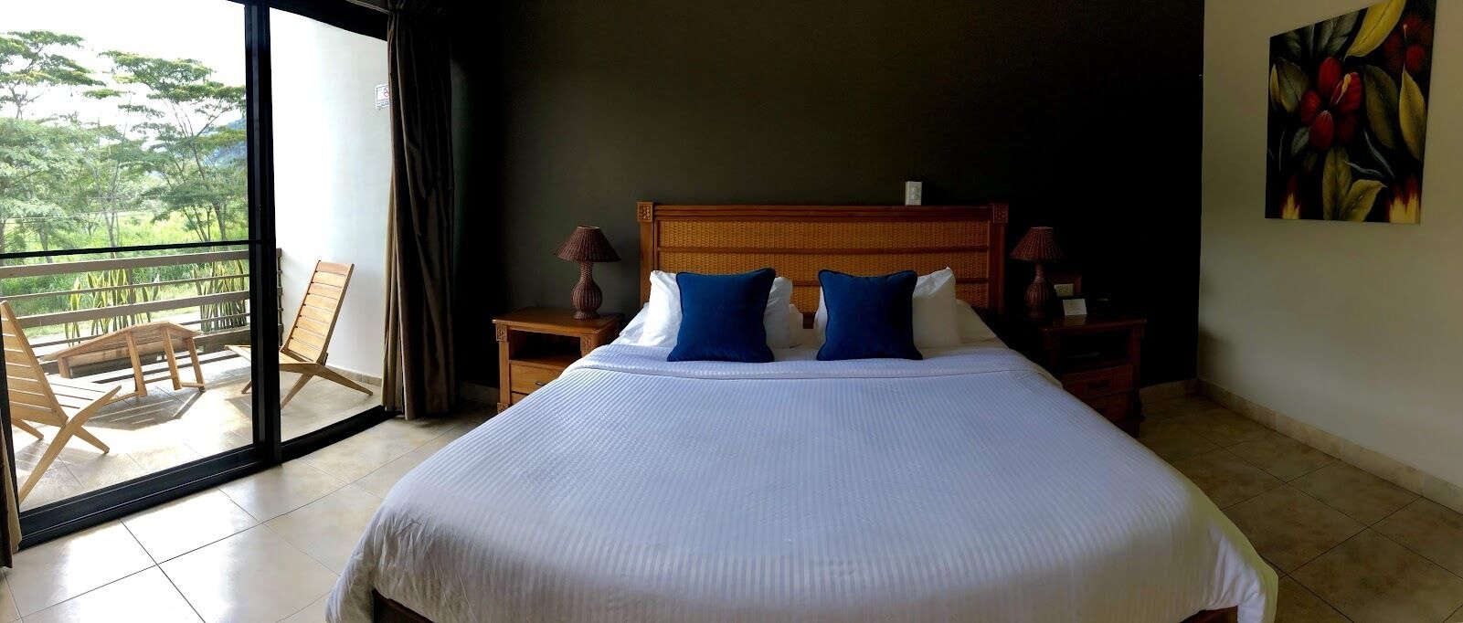 A hotel room with a large bed, two nightstands, a wooden headboard, and a balcony with chairs.