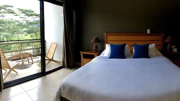 A hotel room with a large bed, two nightstands, a wooden headboard, and a balcony with chairs.