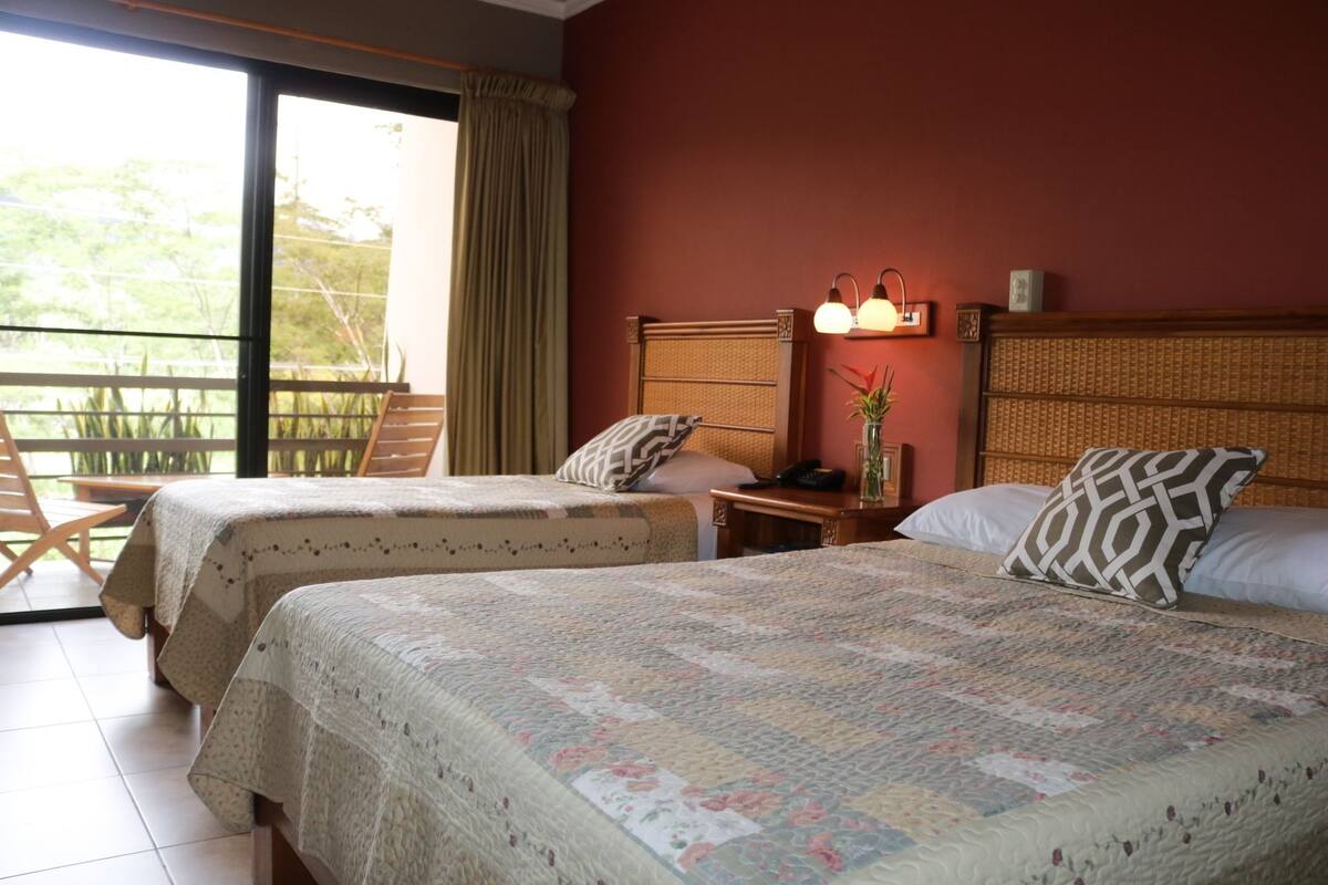 Habitación de hotel con dos camas, un balcón y vistas a la vegetación.