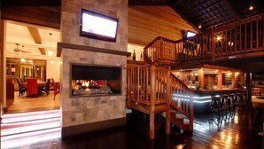 Un interior amplio con chimenea de piedra, escalera de madera y zona de bar.