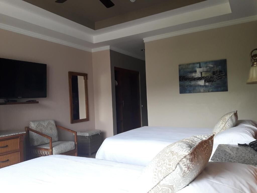 A hotel room with two beds, a television, a chair, a desk, and a painting on the wall.