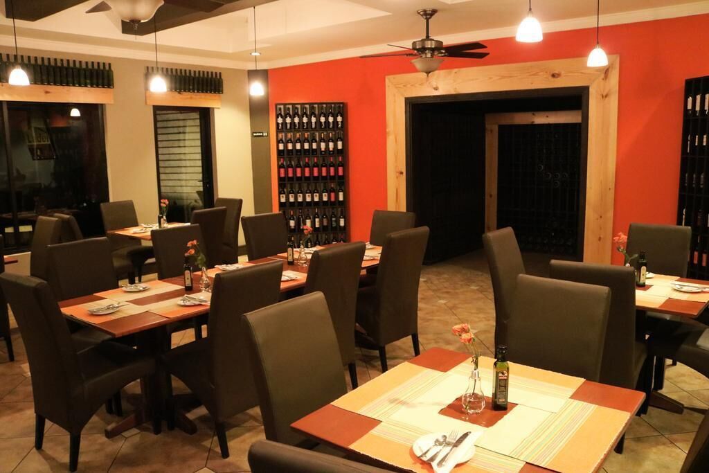 A restaurant with multiple tables and chairs, a wine rack, and a ceiling fan.