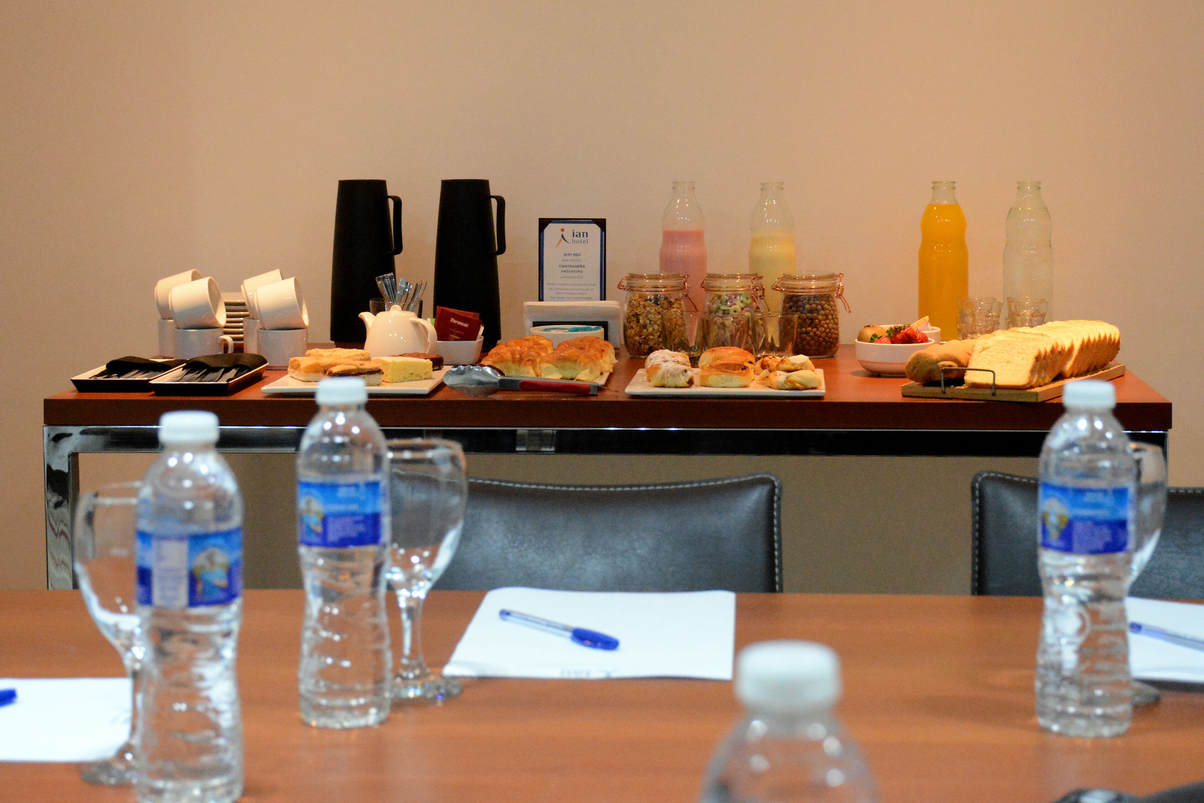 Una mesa de desayuno buffet con diversos alimentos, botellas de agua y una estación de café.