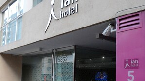 Das Ian Hotel mit Glastür, einem Schild mit der Nummer 5832 und einer rosafarbenen Wand mit dem Hotelnamen.