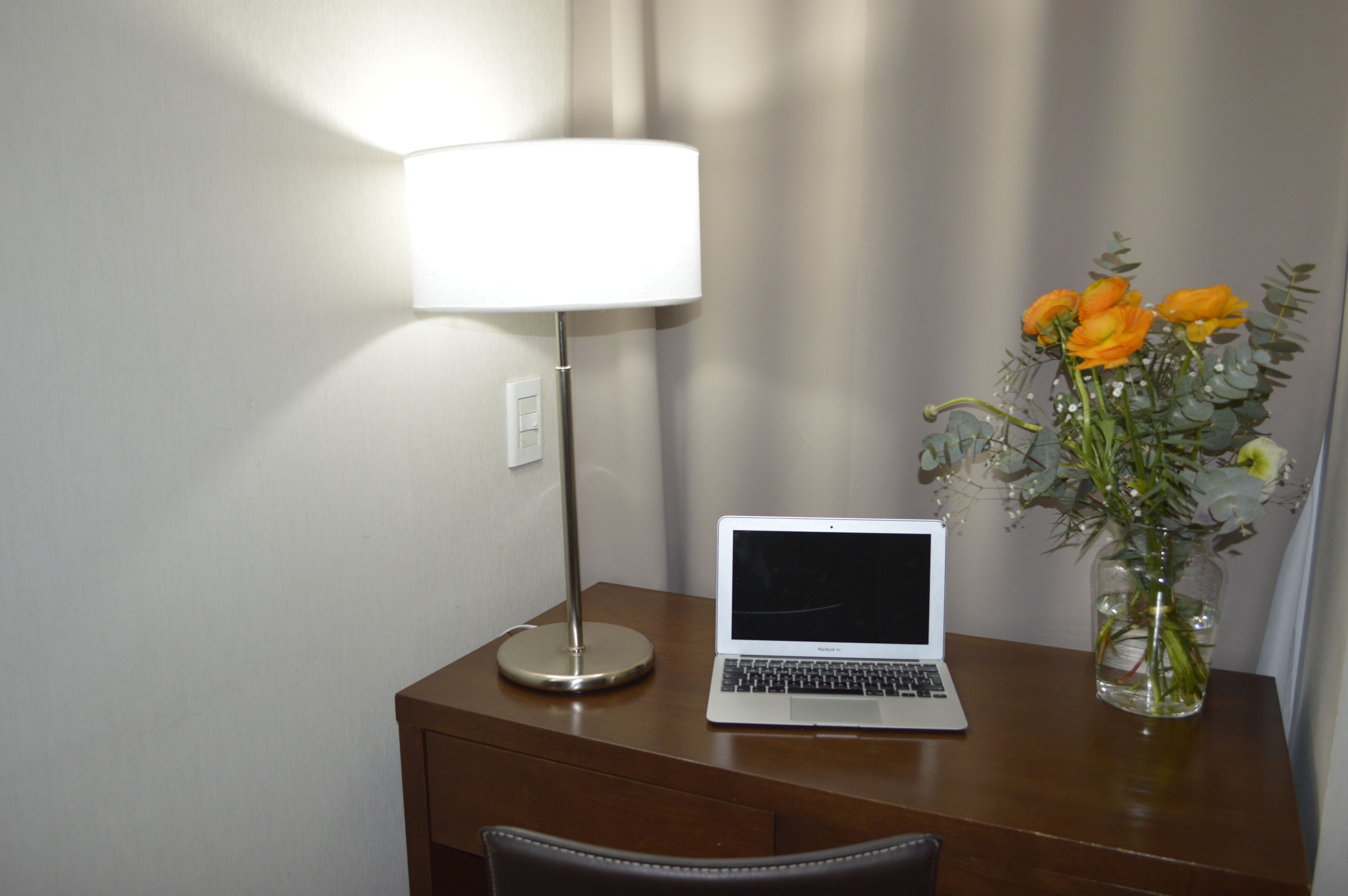 A laptop on a wooden table with a lamp and a vase of flowers.