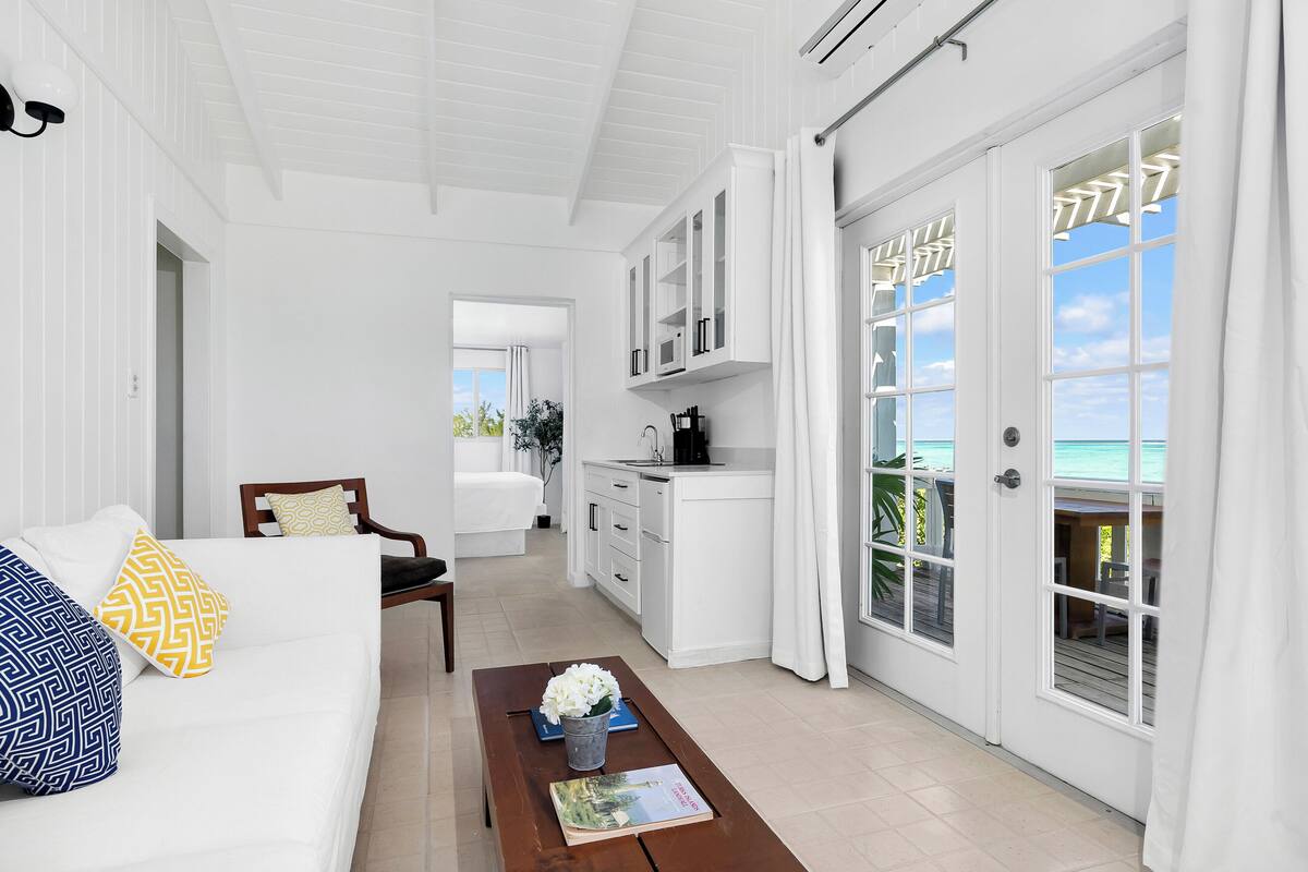 A bright, white interior with a sofa, coffee table, and a view of the ocean through large windows.