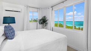 A hotel room with a large bed, a nightstand with a lamp, a potted plant, and a view of the ocean.