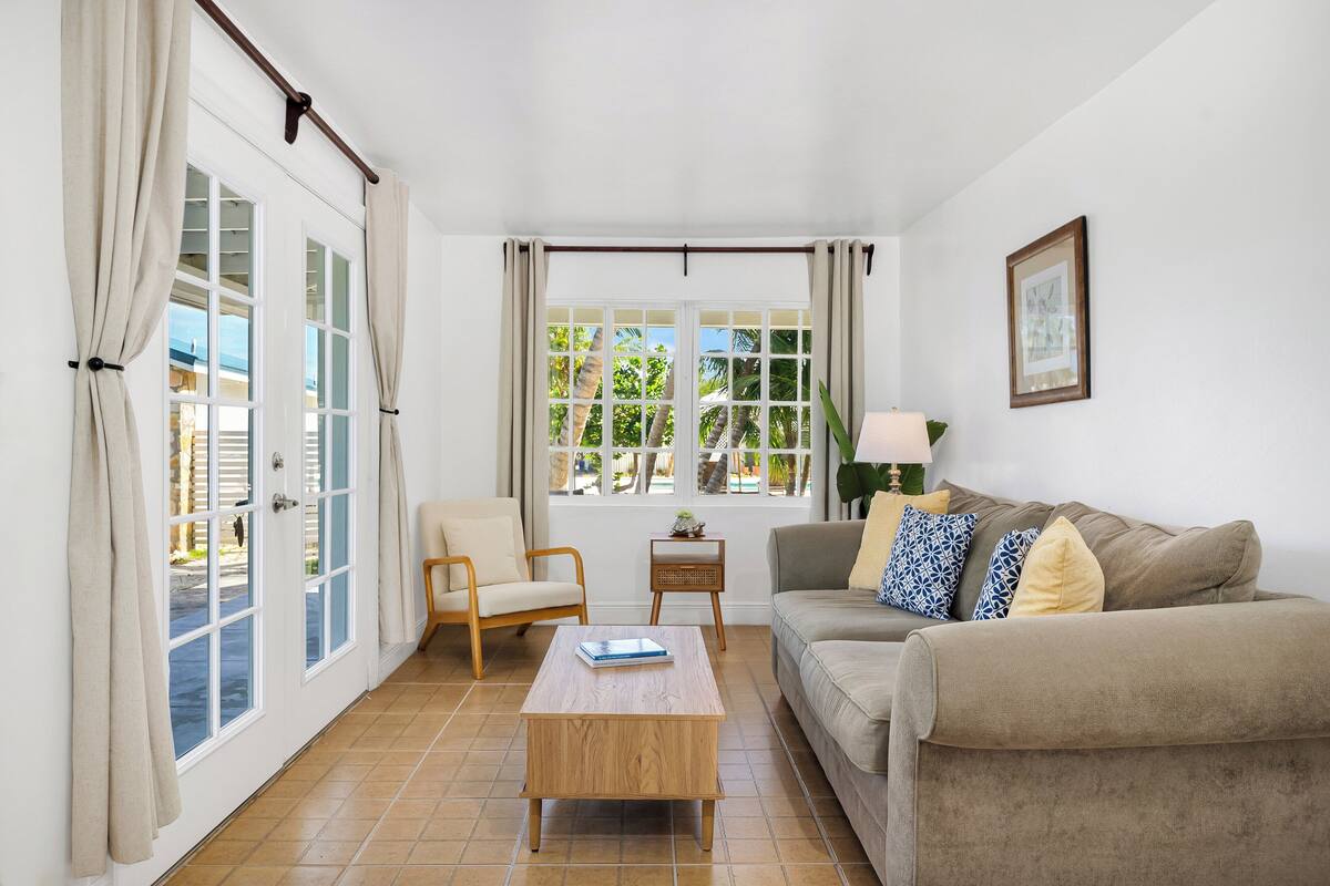 A living room with a sofa, a coffee table, a chair, and a window with curtains.