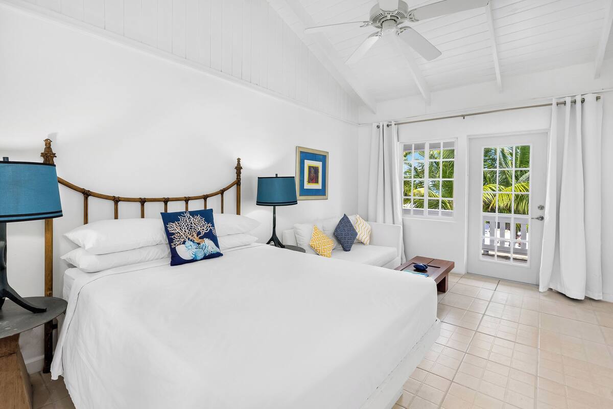 A spacious bedroom with a large bed, a ceiling fan, and a view of the outdoors through a sliding glass door.