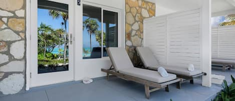 Een overdekt terras met twee lounge stoelen en een stenen muur.