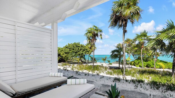 A beachside lounge with white cushioned seating and a view of the ocean.