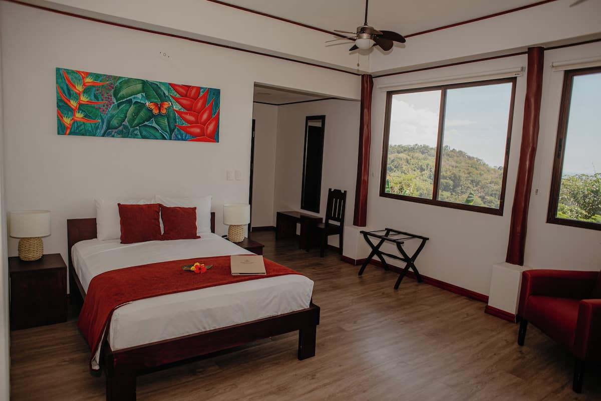 Una habitación de hotel con cama, escritorio, silla, ventana grande y ventilador de techo.