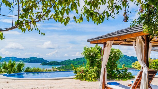 A poolside area with a wooden pergola, lounge chairs, and a view of a mountainous landscape. - Eco Boutique Hotel Vista Las Islas Reserva Natural (Paquera)