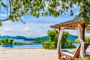 A poolside area with a wooden pergola, lounge chairs, and a view of a mountainous landscape. - Eco Boutique Hotel Vista Las Islas Reserva Natural (Paquera)