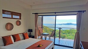 A bedroom with a large bed, a small table with chairs, and a balcony with a view of the ocean. - Eco Boutique Hotel Vista Las Islas Reserva Natural (Paquera)